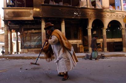 A vendor sweeps broken glass in front of a burned building in the main tourist street of La Paz, Bolivia on Wednesday, October 15 2003. (Associated Press)